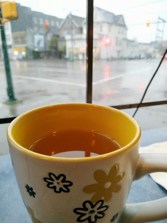 Person sipping tea by a window on a rainy Vancouver afternoon